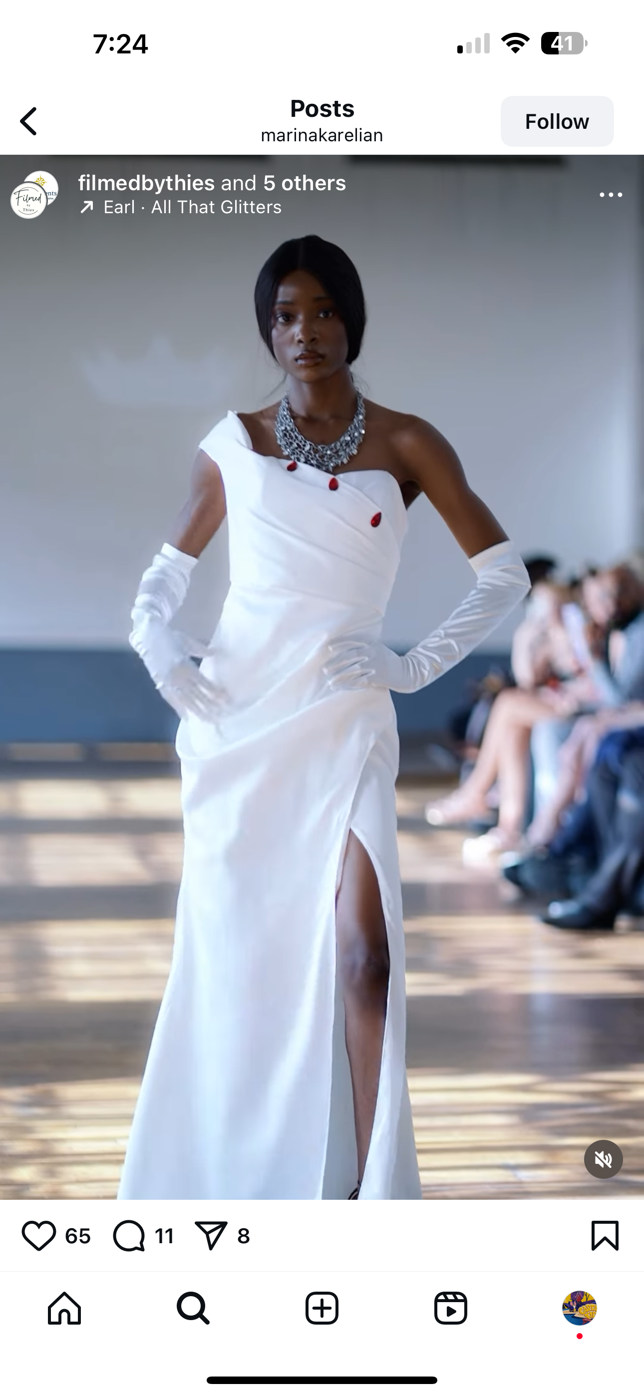 Crafted in lustrous white satin, this striking floor-length gown features an asymmetrical neckline adorned with elegant red button detailing, creating a bold yet timeless silhouette.