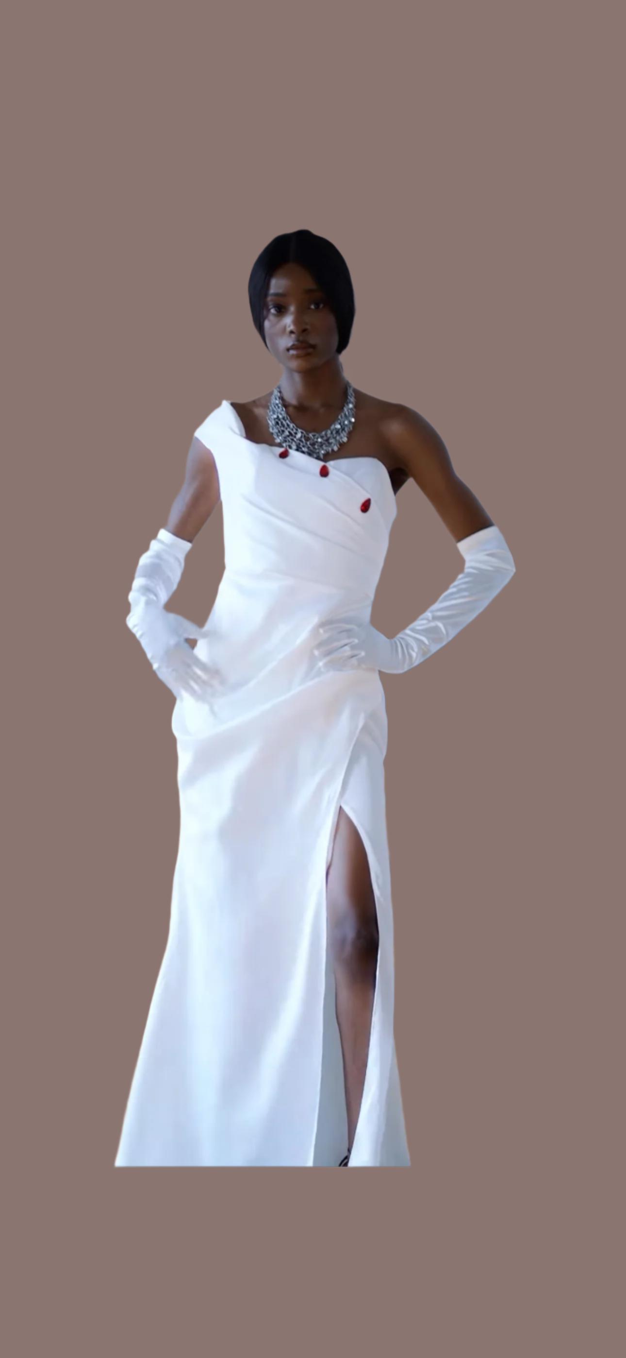 Crafted in lustrous white satin, this striking floor-length gown features an asymmetrical neckline adorned with elegant red button detailing, creating a bold yet timeless silhouette.